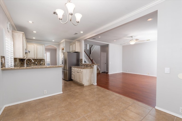 kitchen featuring arched walkways, cream cabinetry, decorative backsplash, ornamental molding, and freestanding refrigerator