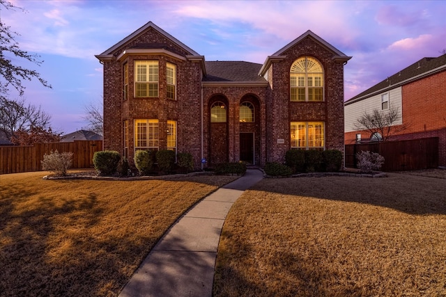 traditional-style home featuring a front yard, fence, and brick siding