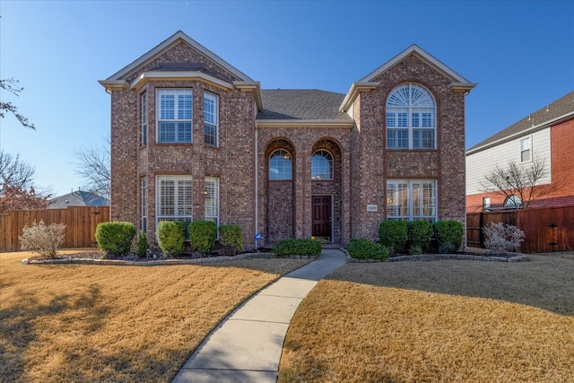 traditional home featuring a front yard, fence, roof with shingles, and brick siding