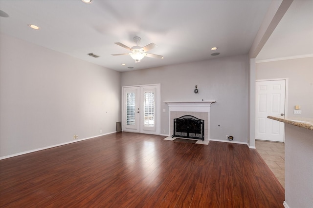 unfurnished living room featuring baseboards, visible vents, a tile fireplace, ceiling fan, and wood finished floors