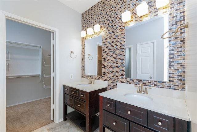 full bathroom featuring a walk in closet, tasteful backsplash, two vanities, and a sink