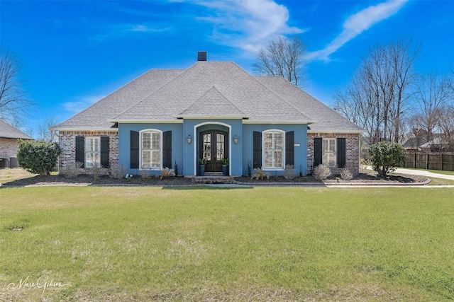 french country style house with roof with shingles, french doors, a front lawn, and brick siding