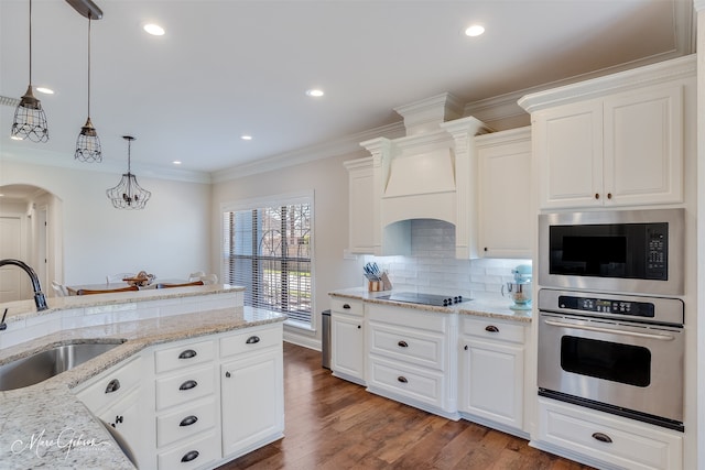 kitchen with arched walkways, ornamental molding, built in microwave, stainless steel oven, and a sink