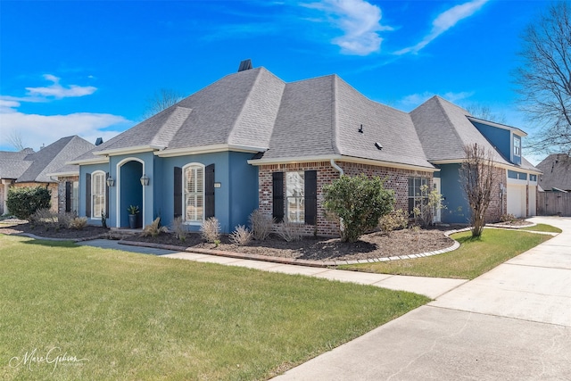 french country home featuring driveway, a garage, a shingled roof, brick siding, and a front yard