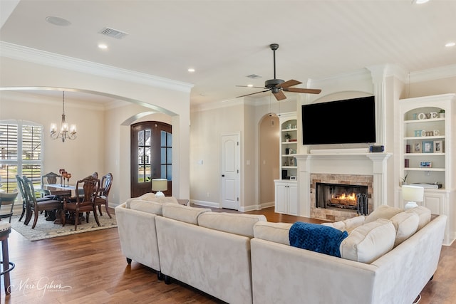 living room featuring a warm lit fireplace, built in features, baseboards, visible vents, and wood finished floors