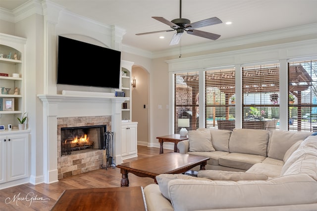 living room with light wood-type flooring, a lit fireplace, built in features, and crown molding