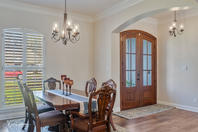 dining space featuring arched walkways, wood finished floors, french doors, ornamental molding, and an inviting chandelier