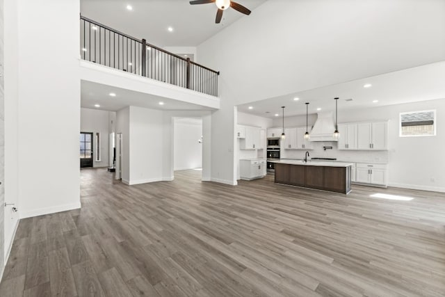 unfurnished living room featuring light wood-style flooring, a high ceiling, baseboards, and a ceiling fan