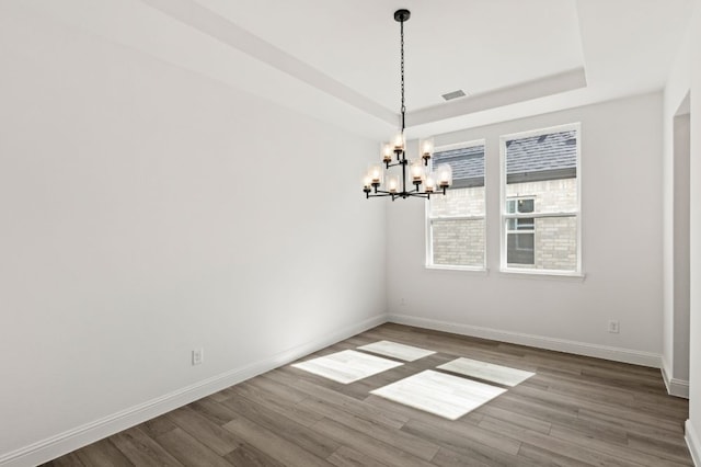 unfurnished dining area with a chandelier, wood finished floors, visible vents, baseboards, and a raised ceiling