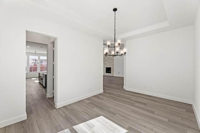 unfurnished dining area with light wood finished floors, baseboards, a raised ceiling, a fireplace, and a chandelier