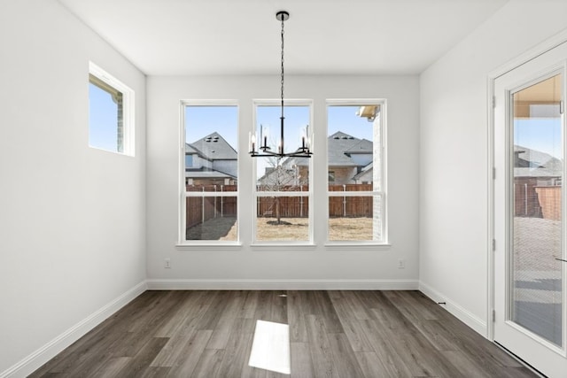 unfurnished dining area featuring an inviting chandelier, wood finished floors, and baseboards