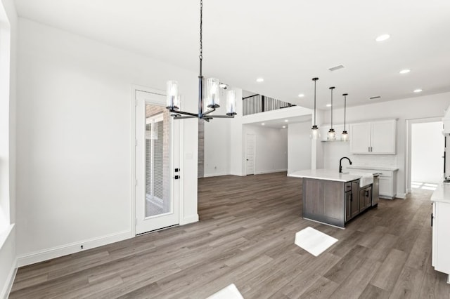 kitchen with a center island with sink, visible vents, open floor plan, wood finished floors, and light countertops