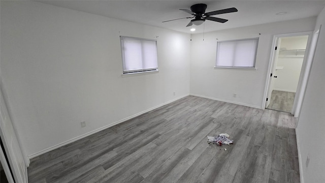 unfurnished bedroom featuring multiple windows, baseboards, a walk in closet, and wood finished floors