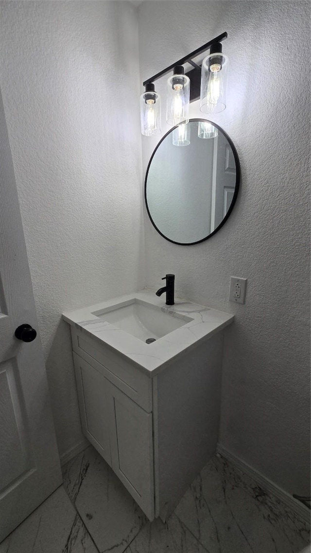 bathroom featuring a textured wall, marble finish floor, vanity, and baseboards