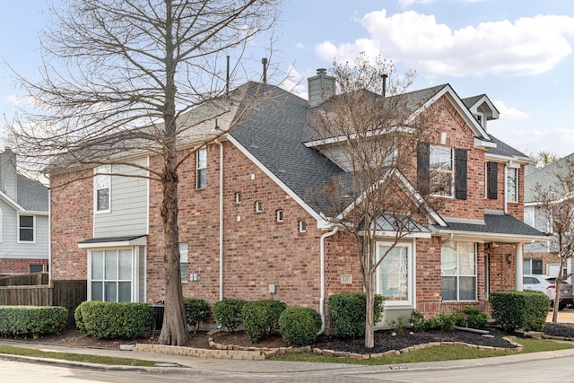 view of front of home with a shingled roof, brick siding, fence, and a chimney