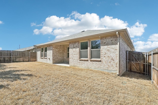 back of house featuring a fenced backyard, brick siding, a patio, and a lawn