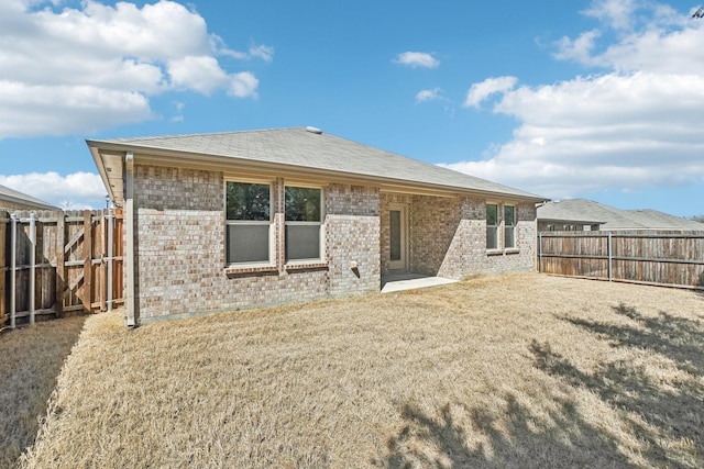 rear view of property featuring a yard, brick siding, and a fenced backyard