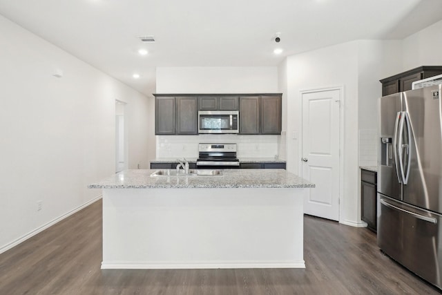 kitchen with dark wood-style floors, stainless steel appliances, a center island with sink, and decorative backsplash