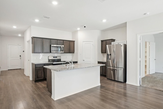 kitchen with dark wood-style floors, stainless steel appliances, dark brown cabinets, and an island with sink