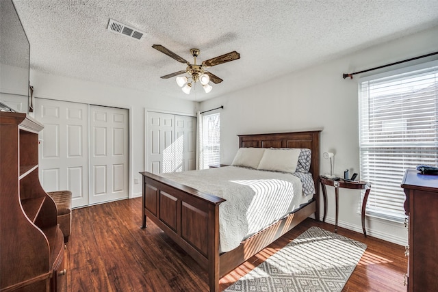 bedroom featuring ceiling fan, dark wood-type flooring, visible vents, baseboards, and two closets