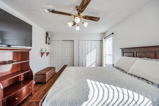 bedroom featuring multiple closets, visible vents, a ceiling fan, a textured ceiling, and wood finished floors