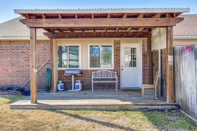 view of exterior entry featuring roof with shingles, fence, and brick siding