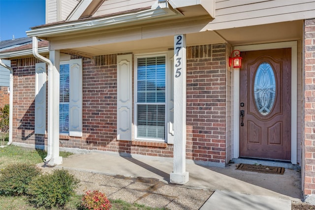 view of exterior entry with covered porch and brick siding