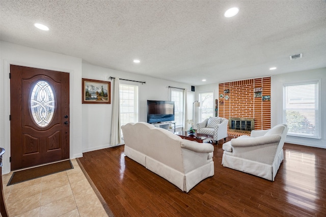 living room featuring a textured ceiling, light wood-style flooring, recessed lighting, visible vents, and a brick fireplace