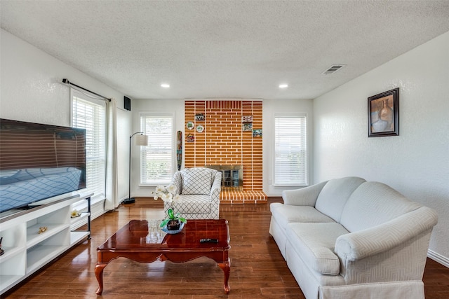 living area featuring a textured ceiling, a textured wall, wood finished floors, visible vents, and a brick fireplace