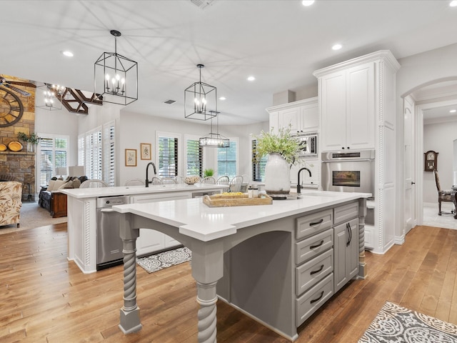 kitchen with open floor plan, a kitchen island with sink, light countertops, a stone fireplace, and light wood-type flooring