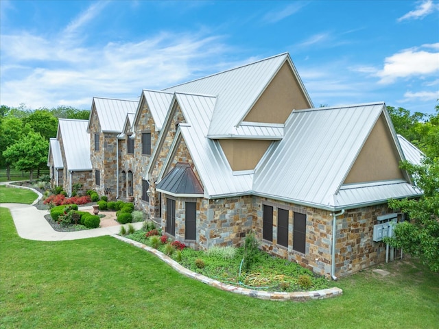 view of front facade featuring stone siding, metal roof, a standing seam roof, a front yard, and stucco siding