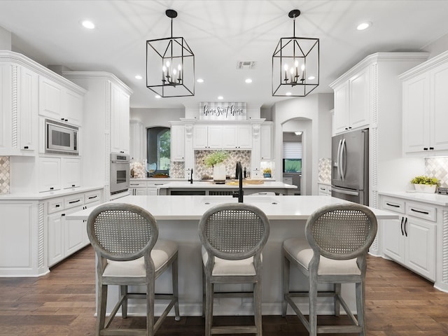 kitchen featuring visible vents, arched walkways, an island with sink, appliances with stainless steel finishes, and a kitchen bar