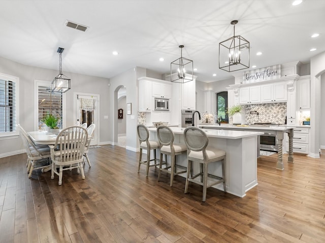 kitchen with arched walkways, light countertops, appliances with stainless steel finishes, tasteful backsplash, and a center island with sink