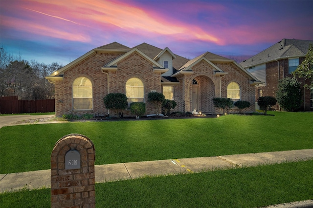 view of front of home with a yard, fence, and brick siding