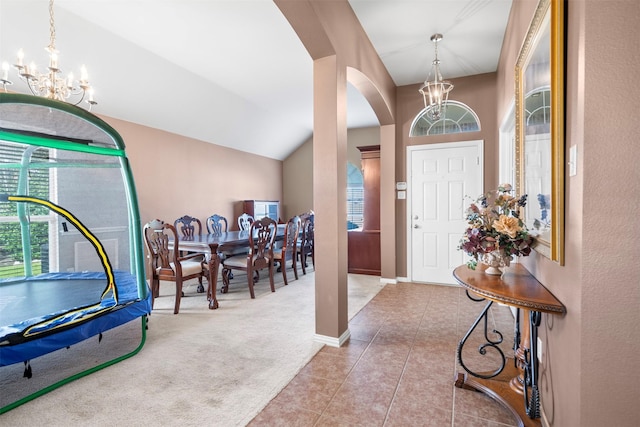 carpeted foyer featuring baseboards, arched walkways, tile patterned floors, an inviting chandelier, and vaulted ceiling