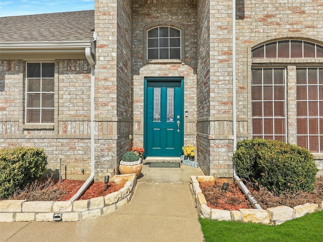 doorway to property featuring brick siding and roof with shingles