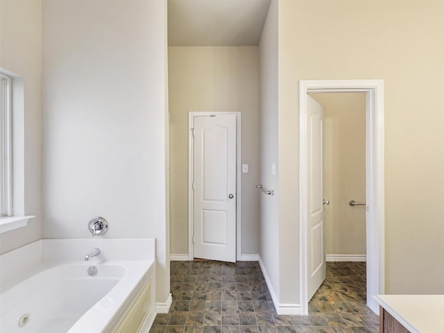 bathroom featuring a whirlpool tub, stone finish flooring, and baseboards