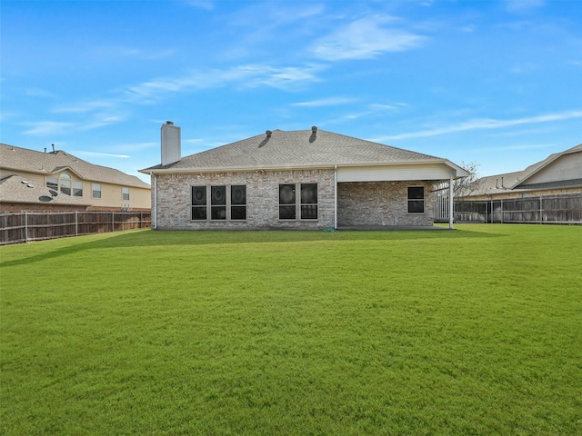 back of property featuring a fenced backyard, a yard, a chimney, and brick siding