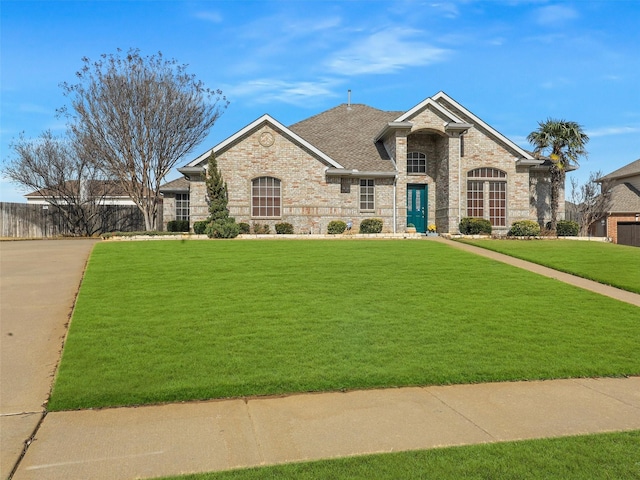 french country home with brick siding, a front yard, fence, and a shingled roof