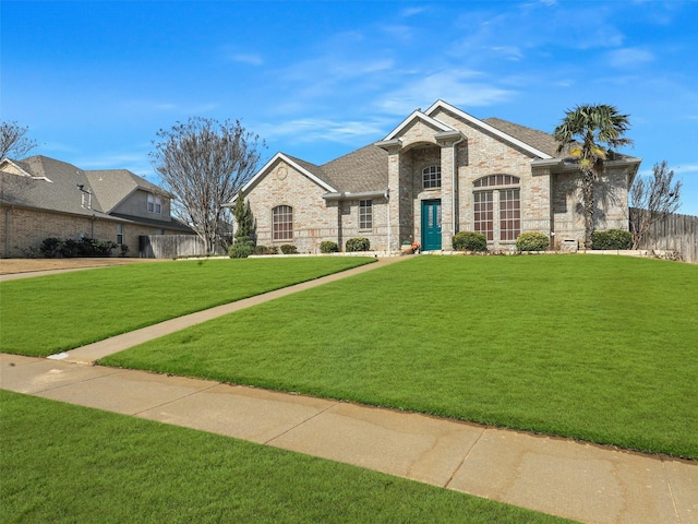 french provincial home with roof with shingles, brick siding, a front lawn, and fence