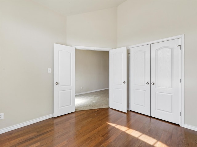 unfurnished bedroom with a closet, a towering ceiling, baseboards, and wood finished floors