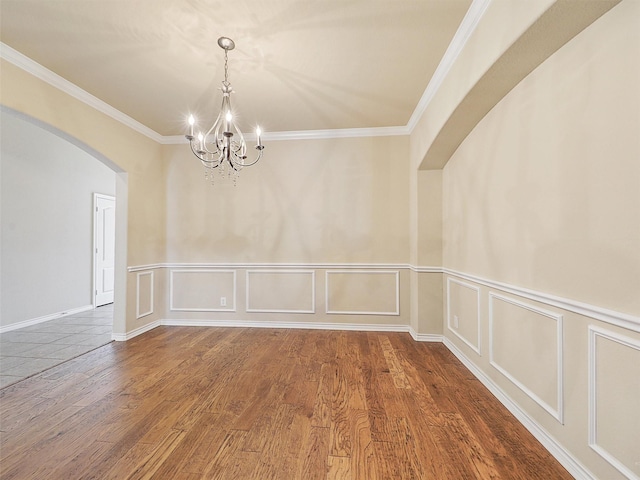 spare room featuring ornamental molding, arched walkways, a decorative wall, and wood finished floors