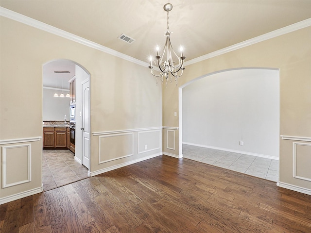 spare room featuring arched walkways, a decorative wall, wood finished floors, visible vents, and crown molding