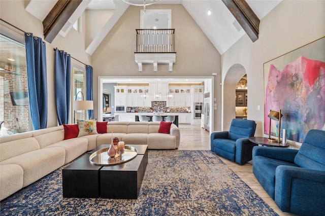 living area with light wood-style floors, arched walkways, beamed ceiling, and high vaulted ceiling