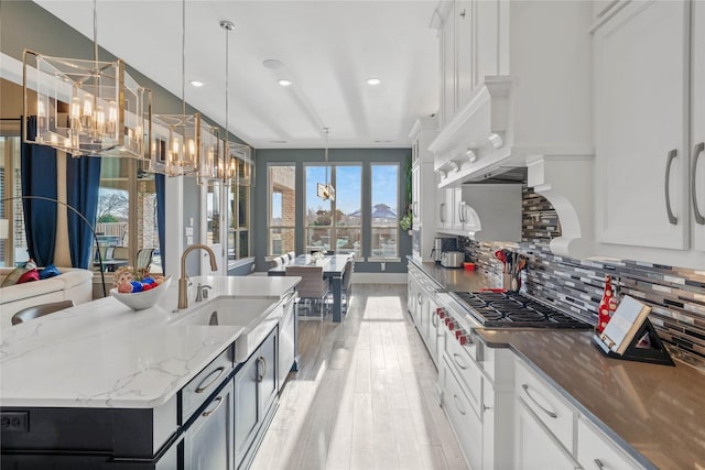 kitchen featuring decorative backsplash, light wood-style flooring, light stone countertops, stainless steel gas cooktop, and a notable chandelier