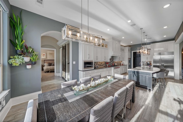 dining room featuring arched walkways, a notable chandelier, visible vents, light wood-style flooring, and baseboards