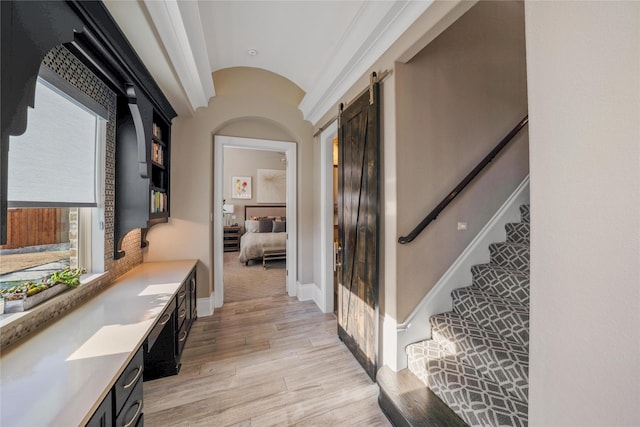 hallway with lofted ceiling, a barn door, baseboards, stairway, and light wood finished floors