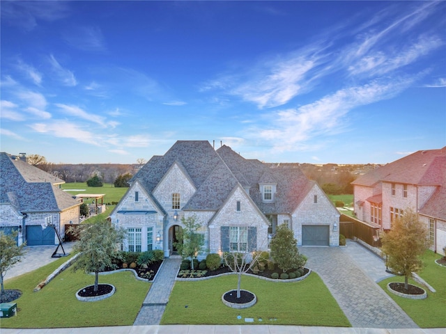 french country style house with a garage, stone siding, decorative driveway, and a front yard