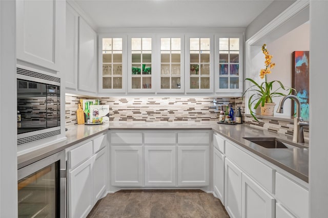 kitchen featuring tasteful backsplash, glass insert cabinets, white cabinets, a sink, and beverage cooler