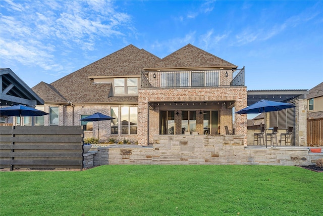 rear view of property featuring a patio area, brick siding, a yard, and a balcony